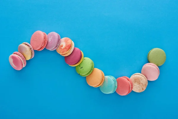Top view of multicolored delicious French macaroons in curved line on blue bright background with copy space — Stock Photo