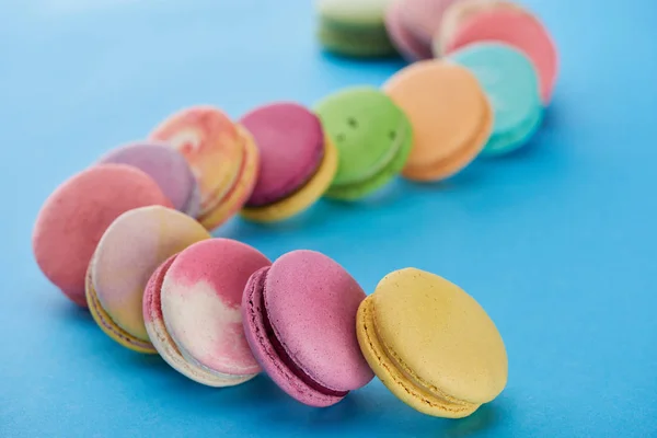 Selective focus of multicolored delicious French macaroons on blue bright background — Stock Photo