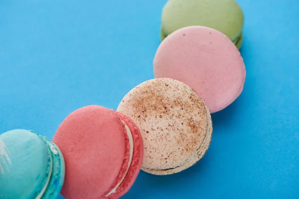 Close up view of multicolored tasty French macaroons on blue bright background — Stock Photo
