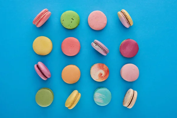 Flat lay com multicoloridos deliciosos macaroons franceses no fundo azul brilhante — Fotografia de Stock