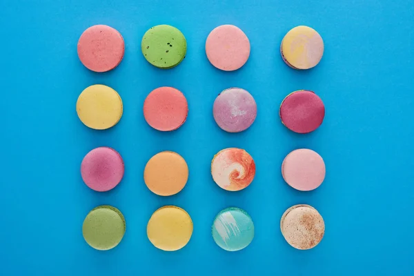 Leigos planos com macaroons franceses saborosos multicoloridos em fundo azul brilhante — Fotografia de Stock