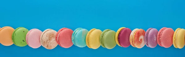 Line of multicolored delicious French macaroons on blue bright background with copy space, panoramic shot — Stock Photo