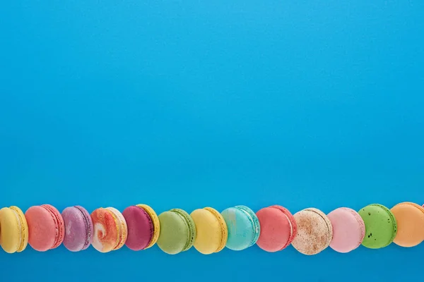 Linha de macaroons franceses deliciosos multicoloridos em fundo azul brilhante com espaço de cópia — Fotografia de Stock