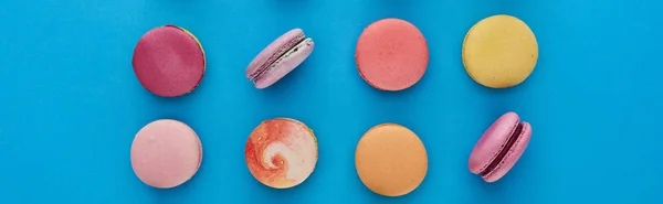 Flat lay com doces deliciosos macaroons franceses no fundo azul brilhante, tiro panorâmico — Fotografia de Stock