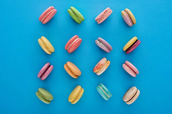 Flat lay com doce multicolorido deliciosos macaroons franceses no fundo azul brilhante — Fotografia de Stock