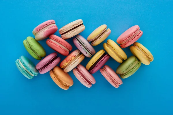 Вид зверху барвисті смачні французькі макаруни на синьому яскравому фоні — стокове фото