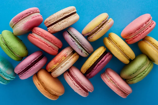 Vista superior de una variedad de deliciosos macarrones franceses sobre fondo azul brillante - foto de stock