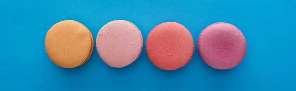 Flat lay with colorful delicious French macaroons on blue bright background, panoramic shot — Stock Photo