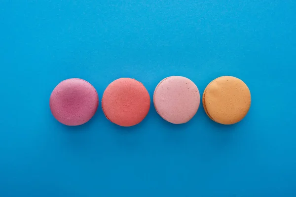 Vue de dessus de délicieux macarons français colorés sur fond bleu vif — Photo de stock