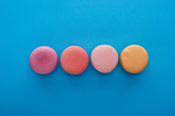 Vista superior de coloridos macarrones franceses deliciosos sobre fondo azul brillante - foto de stock