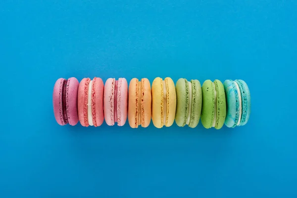 Vista superior de macaroons franceses deliciosos frescos coloridos em linha no fundo brilhante azul — Fotografia de Stock