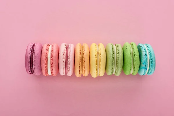Вид зверху барвисті свіжі смачні французькі макаруни в черзі на рожевому фоні — стокове фото