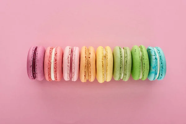 Vista superior de macaroons franceses deliciosos frescos coloridos na linha no fundo rosa — Fotografia de Stock