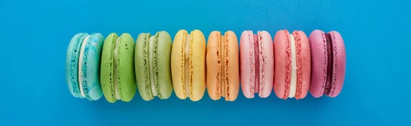 Top view of colorful fresh delicious French macaroons in line on blue bright background, panoramic shot — Stock Photo