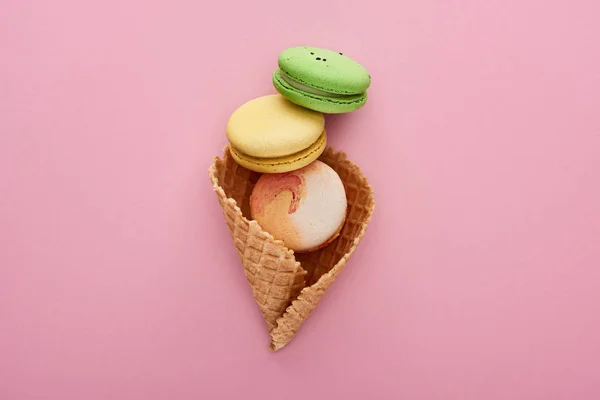 Top view of multicolored delicious French macaroons in crispy waffle cone on pink background — Stock Photo