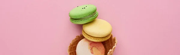 Vista dall'alto di deliziosi macaron francesi multicolori in cono cialda croccante su sfondo rosa, colpo panoramico — Foto stock