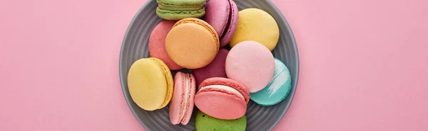 Vista dall'alto di deliziosi macaron francesi multicolori su piatto su sfondo rosa, scatto panoramico — Foto stock