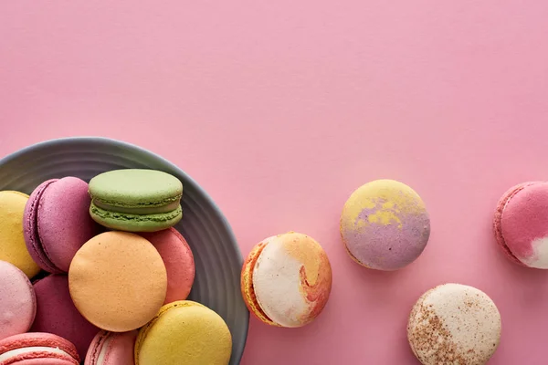 Placa com macaroons franceses saborosos multicoloridos no fundo rosa — Fotografia de Stock