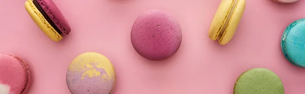 Pattern of multicolored delicious French macaroons scattered on pink background, panoramic shot — Stock Photo