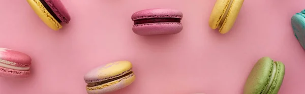Pattern of multicolored fresh French macaroons scattered on pink background, panoramic shot — Stock Photo