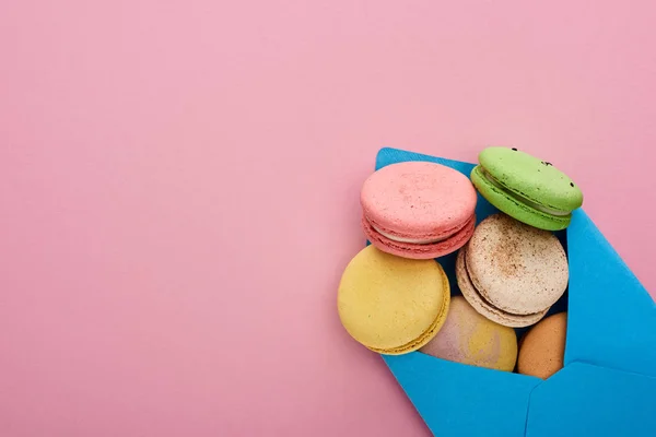 Vista dall'alto di deliziosi macaron francesi multicolori in busta postale blu su sfondo rosa con spazio per la copia — Foto stock