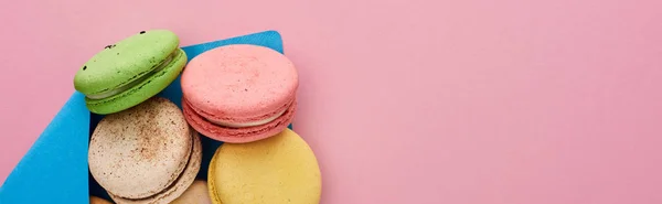 Vista dall'alto di deliziosi macaron francesi multicolori in busta postale blu su sfondo rosa con spazio copia, scatto panoramico — Foto stock