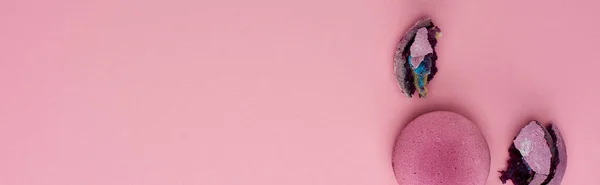 Вид зверху розбили і цілу смачні фіолетові французькі макаруни на рожевому тлі з копіюванням простору, панорамний постріл — стокове фото
