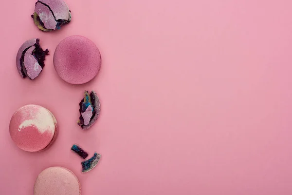 Vista dall'alto di macaron francesi frantumati e interi viola su sfondo rosa con spazio per la copia — Foto stock