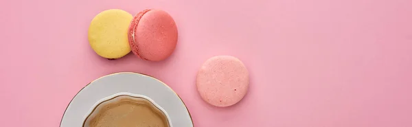 Top view of delicious French macaroons near coffee in cup on saucer on pink background, panoramic shot — Stock Photo