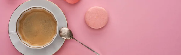 Top view of delicious French macaroons near coffee with silver spoon on pink background with copy space, panoramic shot — Stock Photo