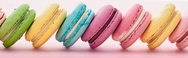 Row of delicious French macaroons of different flavors on pink background, panoramic shot — Stock Photo