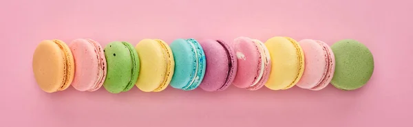 Fila de deliciosos macarrones franceses coloridos de diferentes sabores sobre fondo rosa, plano panorámico - foto de stock