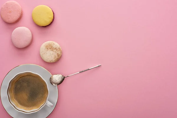 Draufsicht auf köstliche französische Makronen in der Nähe von Kaffee mit Löffel auf rosa Hintergrund mit Kopierfläche — Stockfoto