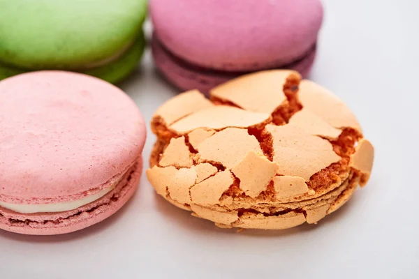 Vista de perto de macaroons franceses coloridos doces de sabores diferentes com um esmagado no fundo branco — Fotografia de Stock