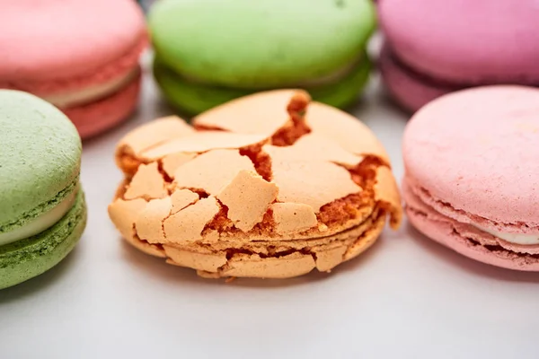 Vista de perto de macaroons franceses coloridos de sabores diferentes com esmagado um no fundo branco — Fotografia de Stock