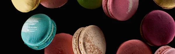 Top view of scattered delicious colorful French macaroons of different flavors isolated on black, panoramic shot — Stock Photo
