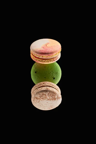 Vista superior de tres deliciosos macarrones franceses coloridos de diferentes sabores aislados en negro - foto de stock