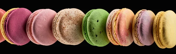 Row of delicious colorful French macaroons of different flavors isolated on black, panoramic shot — Stock Photo