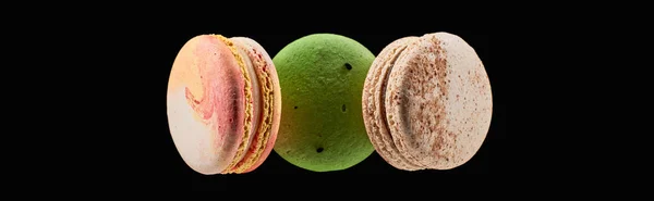Vista superior de tres deliciosos macarrones franceses coloridos de diferentes sabores aislados en negro, plano panorámico - foto de stock
