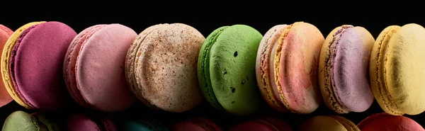 Row of colorful French macaroons of different flavors isolated on black, panoramic shot — Stock Photo