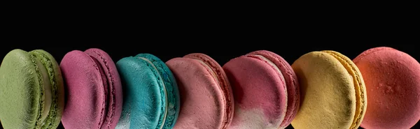 Row of tasty colorful French macaroons of different flavors isolated on black, panoramic shot — Stock Photo