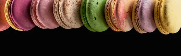 Row of tasty colorful French macaroons of different flavors isolated on black with copy space, panoramic shot — Stock Photo