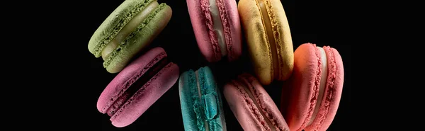 Top view of delicious fresh colorful French macaroons of different flavors isolated on black, panoramic shot — Stock Photo