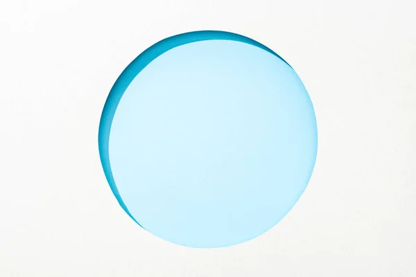 Cut out round hole in white paper on light blue colorful background — Stock Photo