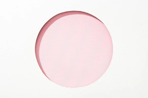 Recortar agujero redondo en papel blanco sobre fondo de rayas de color rosa y blanco - foto de stock