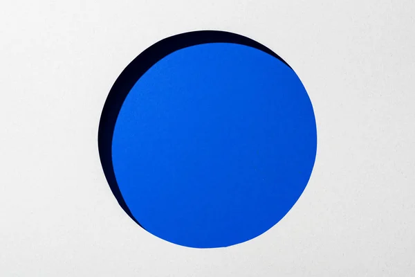 Cut out round hole in white paper on electric blue background — Stock Photo