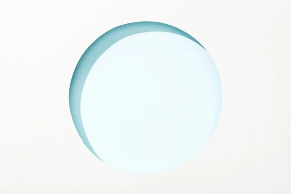 Cut out round hole in white paper on light blue background — Stock Photo