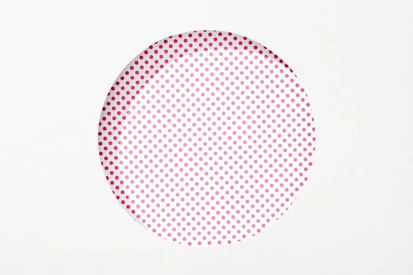 Recortar agujero redondo en papel blanco sobre fondo punteado rosa y blanco - foto de stock