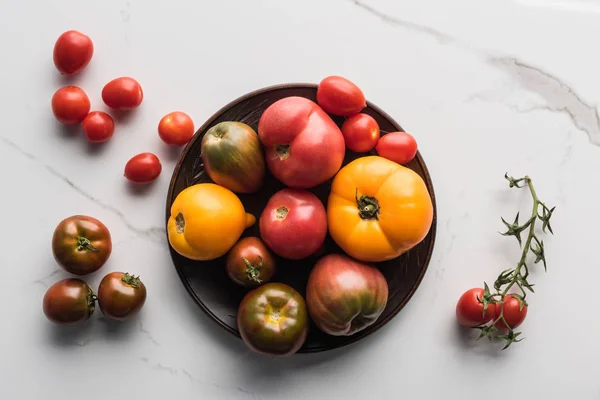 Vista superior de tomates em placa de madeira perto de tomates espalhados na superfície de mármore — Fotografia de Stock