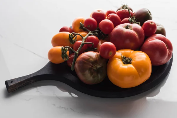 Différentes tomates sur la casserole à pizza en bois sur la surface de marbre — Photo de stock